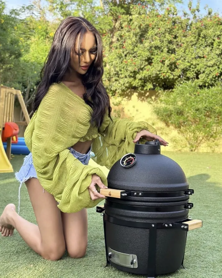 A woman kneeling on the lawn beside a black table-top kamado
