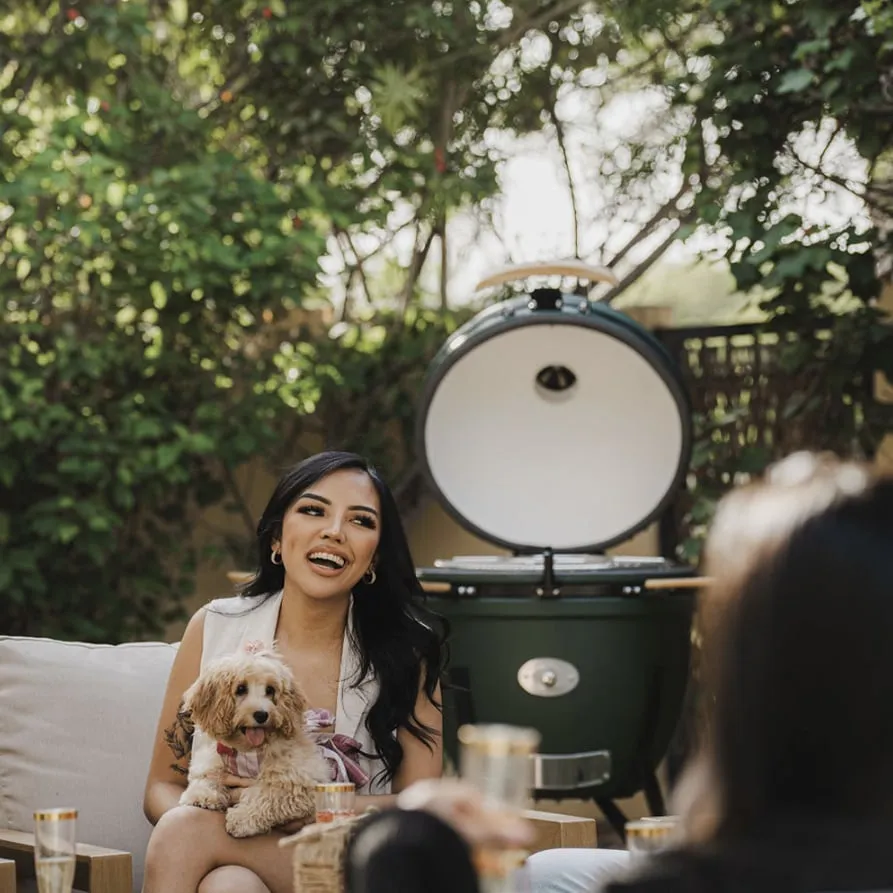 A woman and her dog relaxing beside an open green kamado