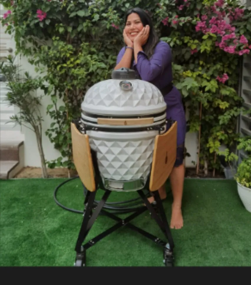 A smiling woman leaning on a white diamond-pattern kamado in a garden