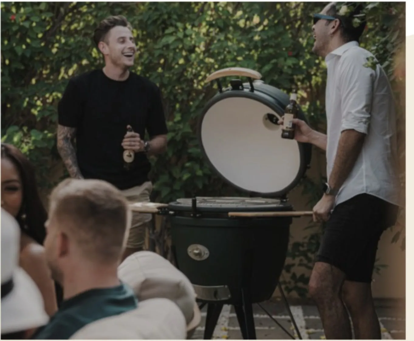 Friends laughing around an open green kamado in a garden